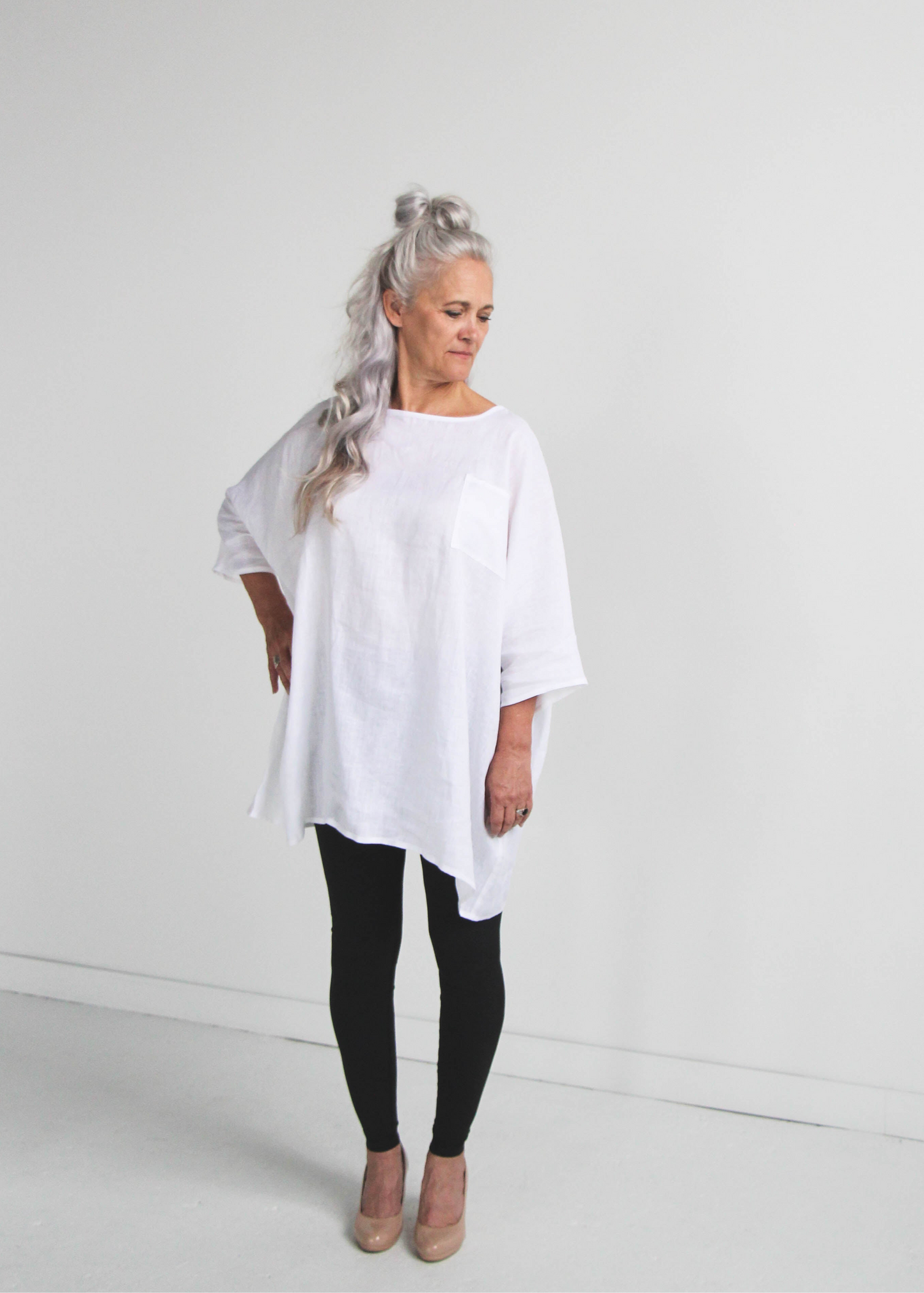 Woman wearing a white linen oversized tunic top and black leggings on a plain background