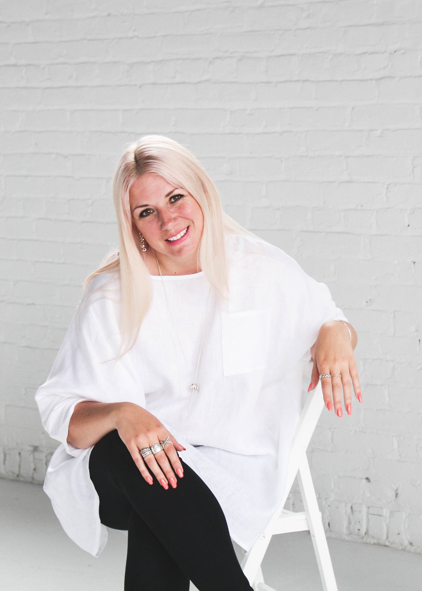 Woman in a white shirt sitting on a chair against a white brick wall.