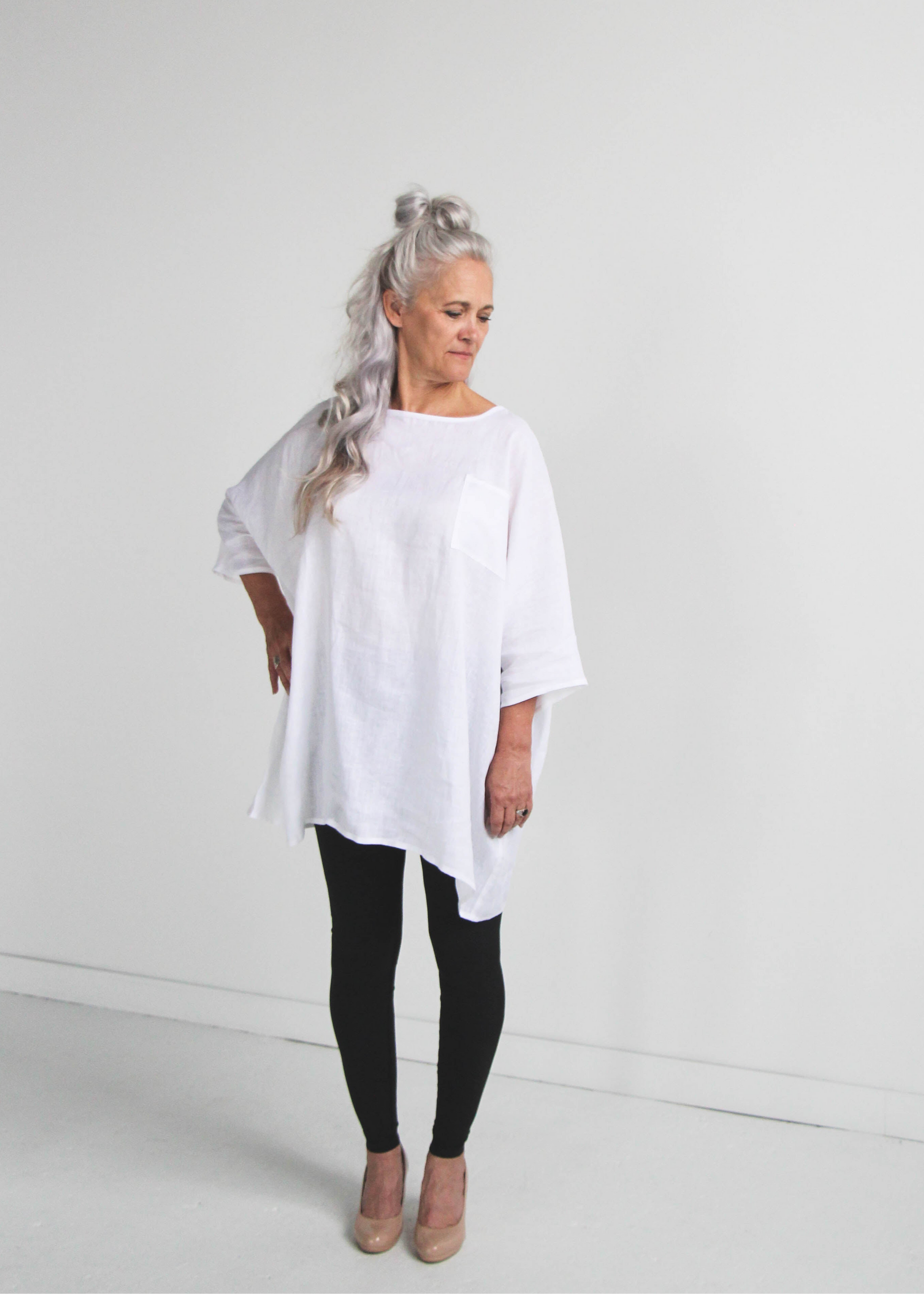 Woman wearing a white linen oversized tunic top and black leggings on a plain background